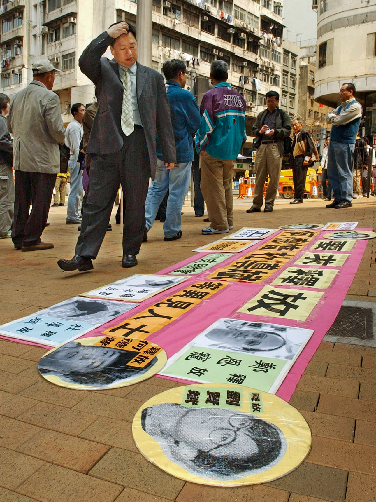 people stand on the street where a banner with the faces of Chinese political prisoners is spread on the ground